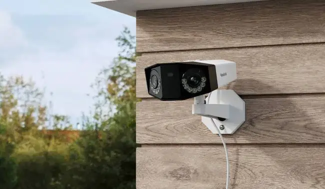 Outdoor security camera mounted on wooden wall with greenery in background