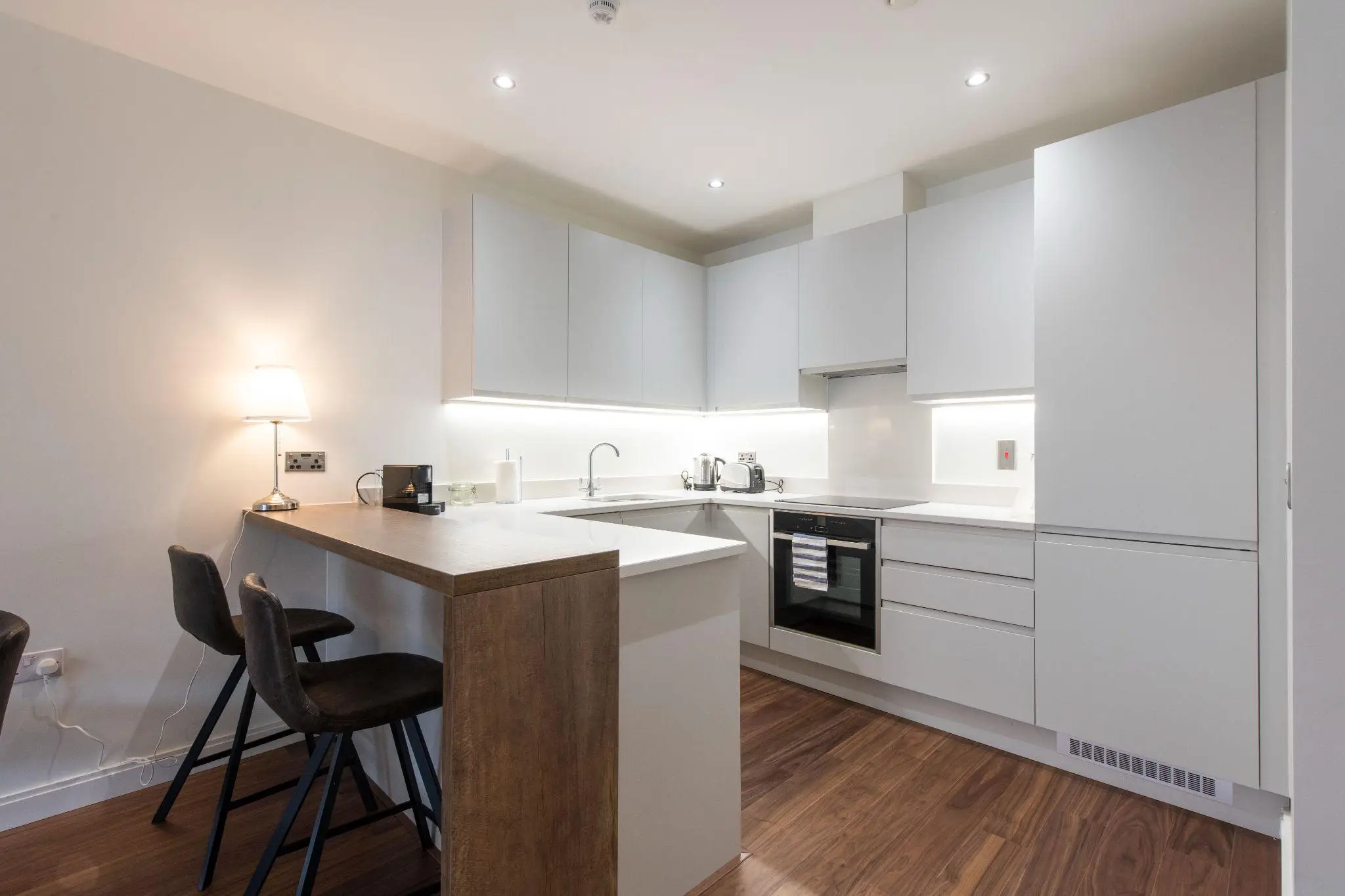 Modern kitchen with white cabinets, wood flooring, and a small breakfast bar under warm lighting