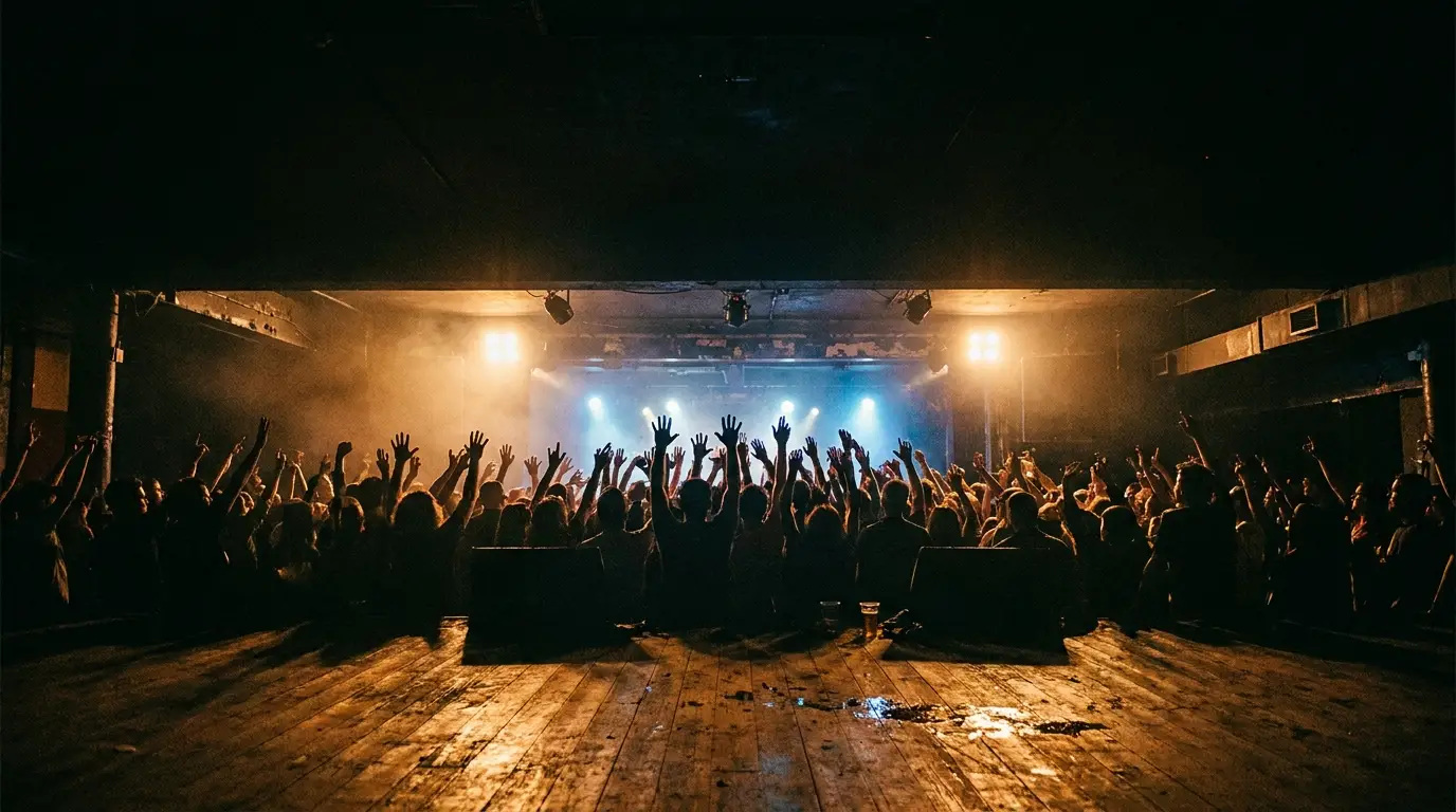 Audience with raised hands at indoor music concert under colorful stage lights