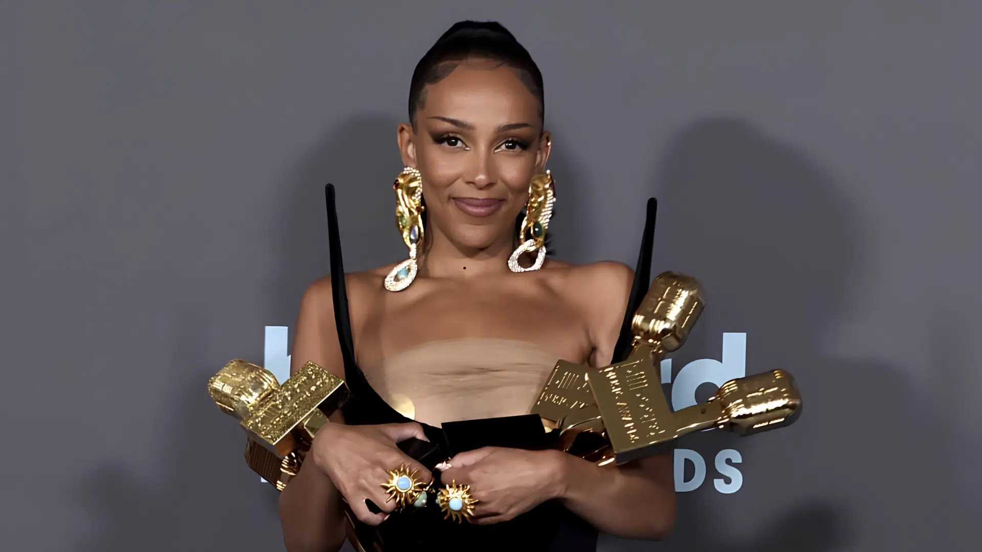 doja cat posing with multiple grammy awards at a red carpet event while wearing a strapless outfit and statement earrings