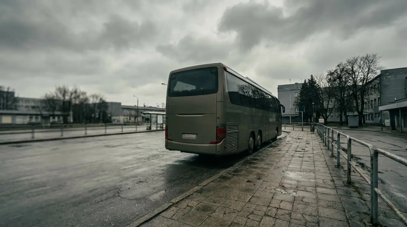 Parked grey coach bus on deserted urban street under overcast sky