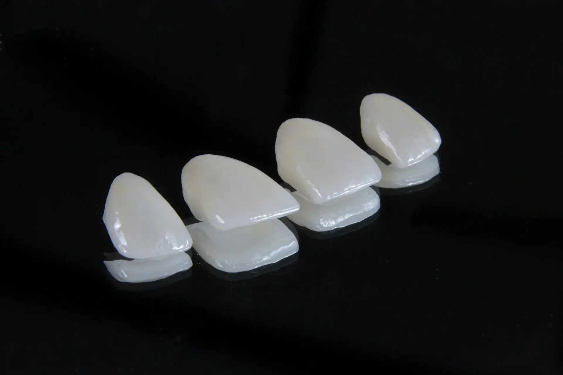 Four dental veneers displayed on a reflective black surface