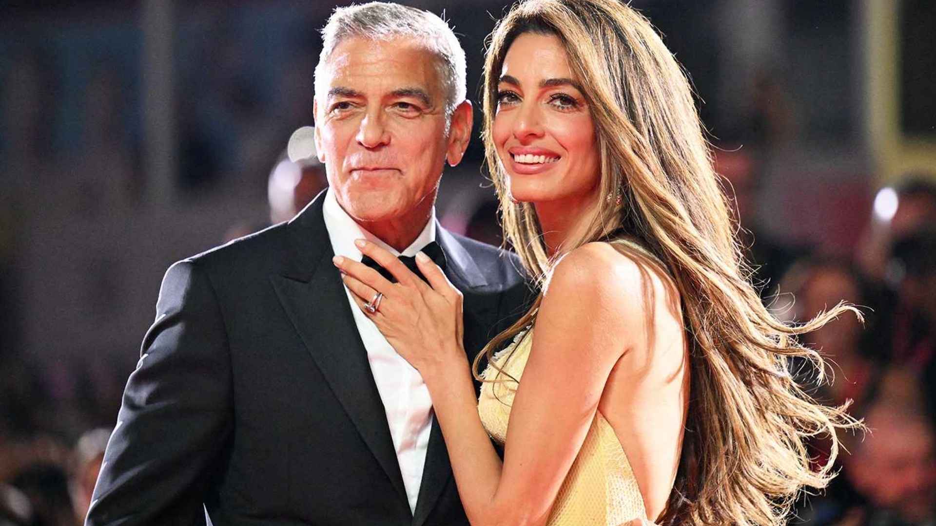George Clooney and Amal Clooney together at a formal event with evening outfits and warm lighting creating a classic portrait scene