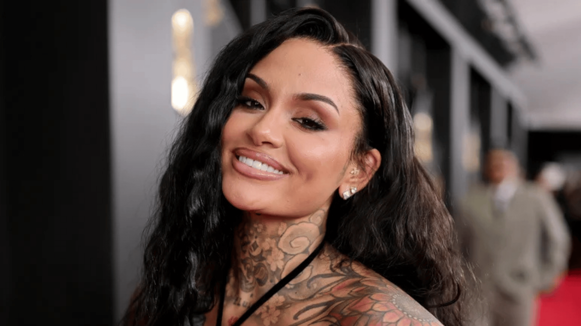 kehlani smiling at an event with long black hair and visible neck tattoos shown.