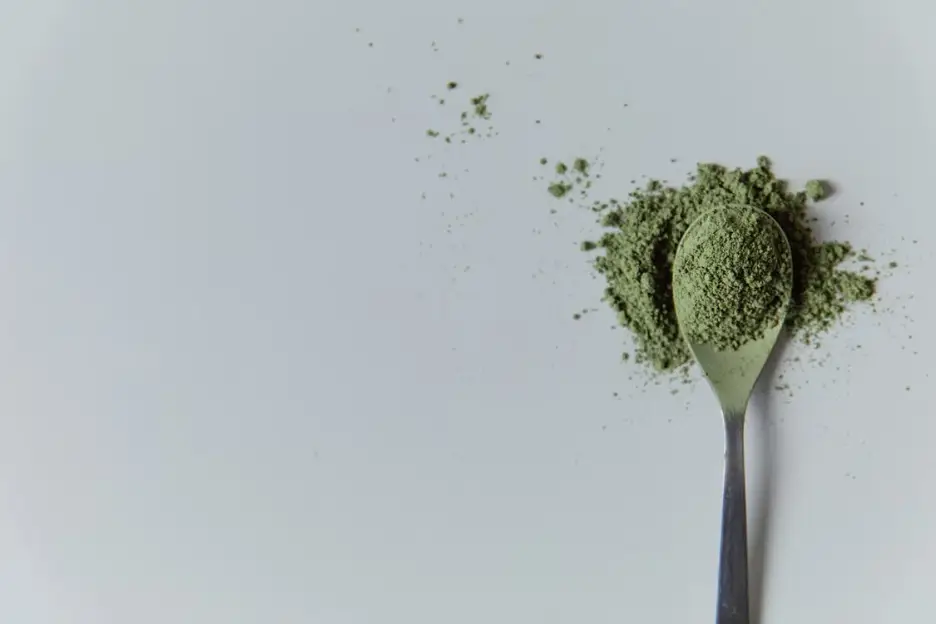 Silver spoon with green powder on a white surface
