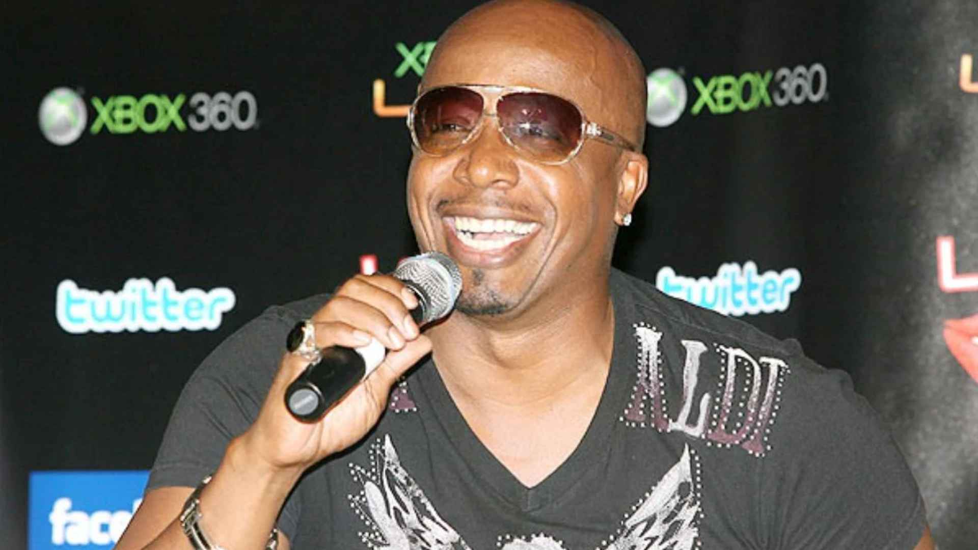 Hammer posing with crossed arms in a black outfit and sunglasses during a vintage studio photoshoot