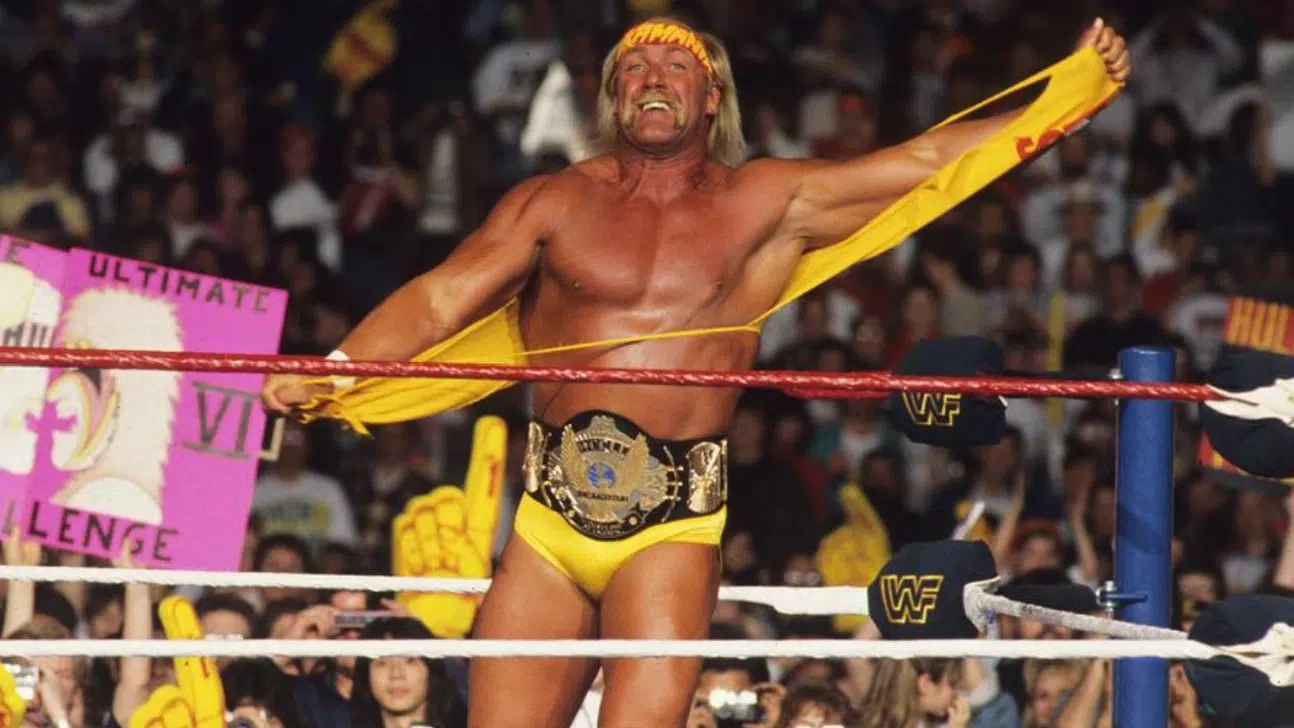hulk hogan in a wrestling ring wearing yellow gear and holding his shirt with a title belt