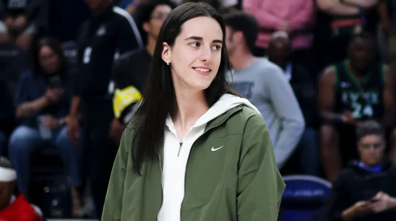 caitlin clark standing courtside in a green nike jacket with spectators blurred in the background