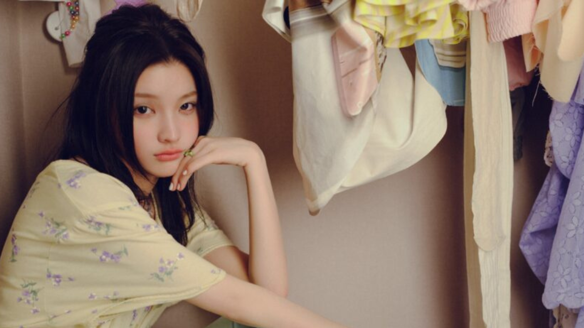 iroha of illit sitting beside hanging clothes
