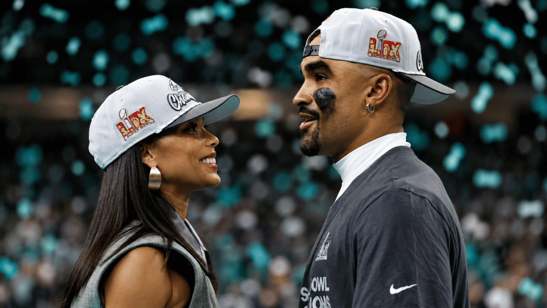 Jalen Hurts and Bry Burrows smiling at each other while celebrating after the Super Bowl victory wearing championship caps