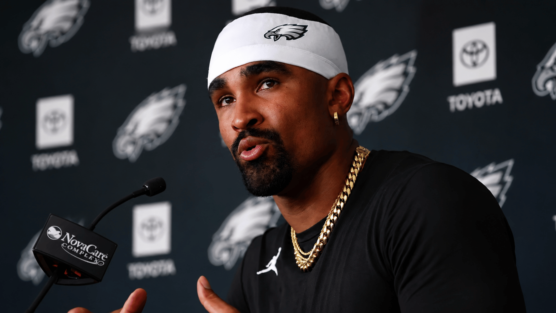 Jalen Hurts speaking at a Philadelphia Eagles press conference while wearing a white team headband and black athletic shirt