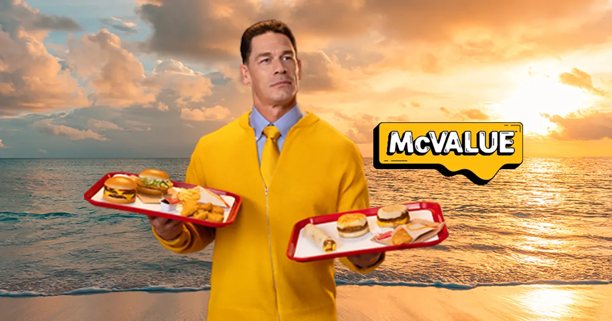 john cena holding fast food trays in a yellow outfit during a mcdonalds mcvalue campaign by the beach