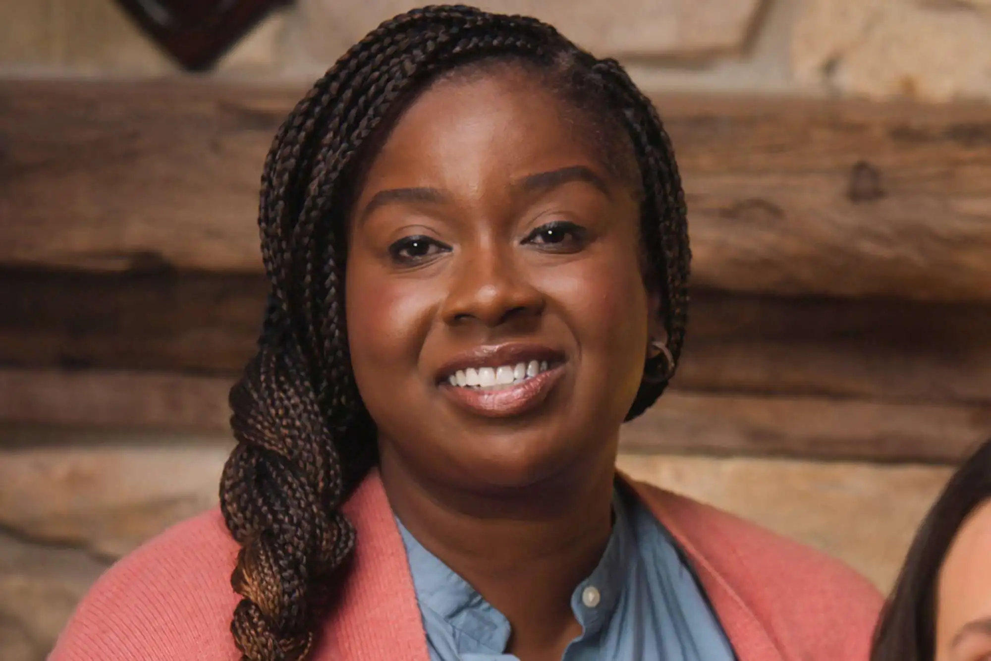 laniss smiling with braided hair wearing a pink cardigan during a company retreat scene