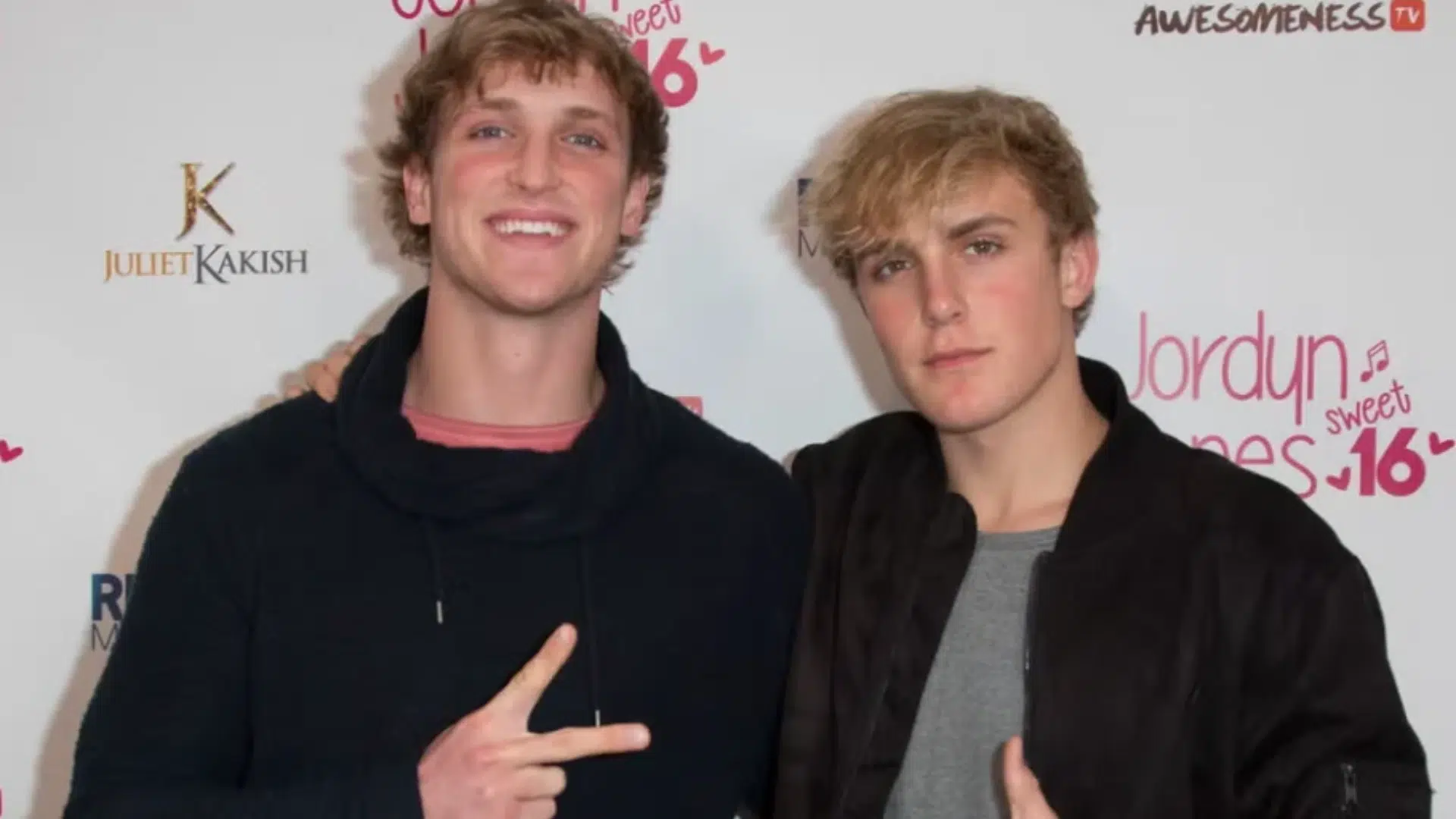 Logan Paul and Jake Paul posing together at a red carpet event, both dressed in black outerwear.