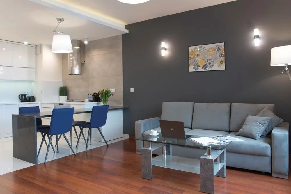 Modern living room and kitchen with gray sofa, glass coffee table, and blue chairs in open-plan space