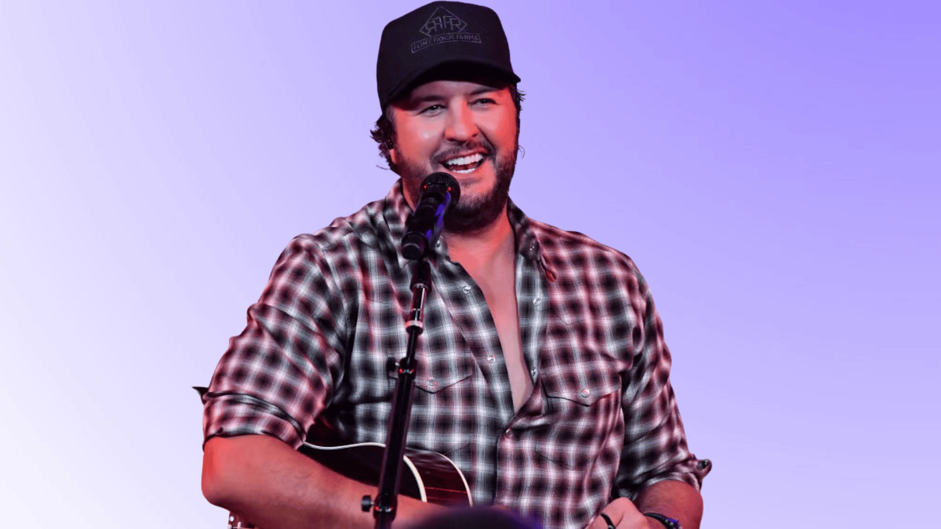 luke bryan singing into a microphone while holding a guitar on stage