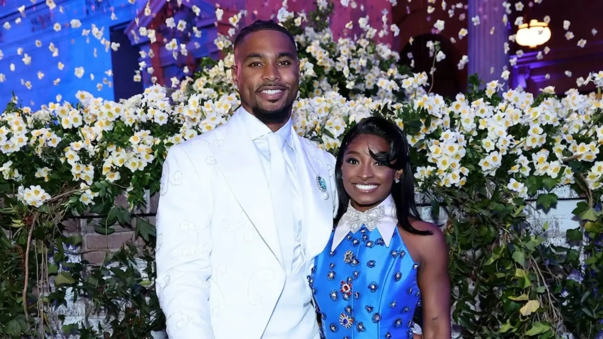 man and woman posing together at a formal event surrounded by white flowers and colorful lights
