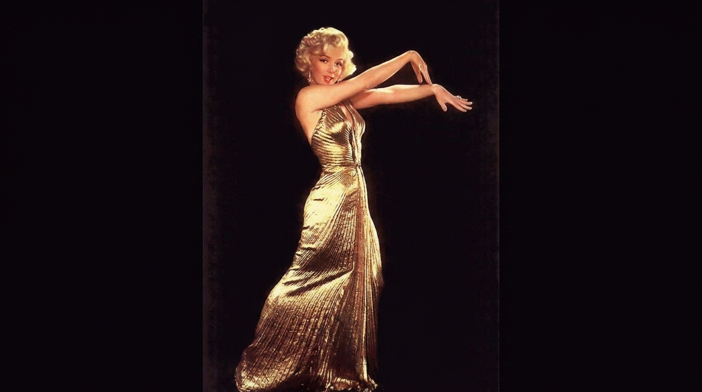 marilyn monroe standing in a fitted metallic gold evening gown during an elegant old hollywood studio portrait