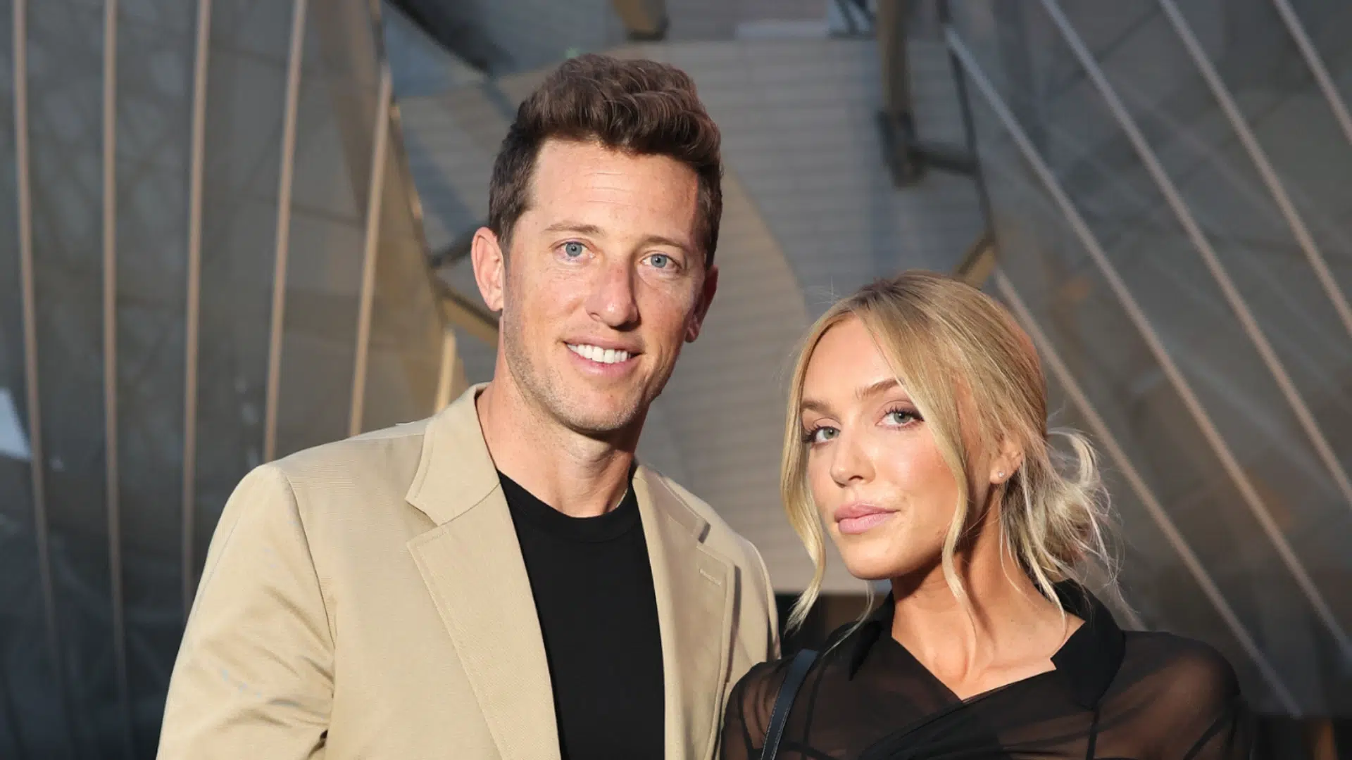 Matt Kaplan in a tan blazer and Alex Cooper in black pose together at a public event