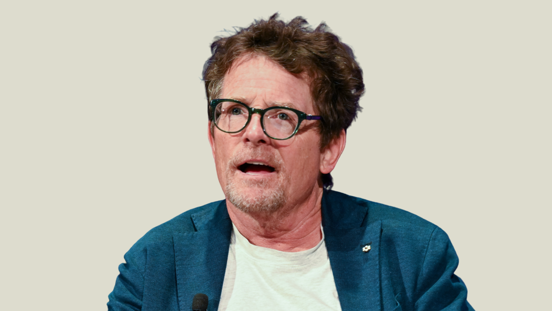 michael j. fox wearing glasses and a blue blazer, speaking into a microphone at an event