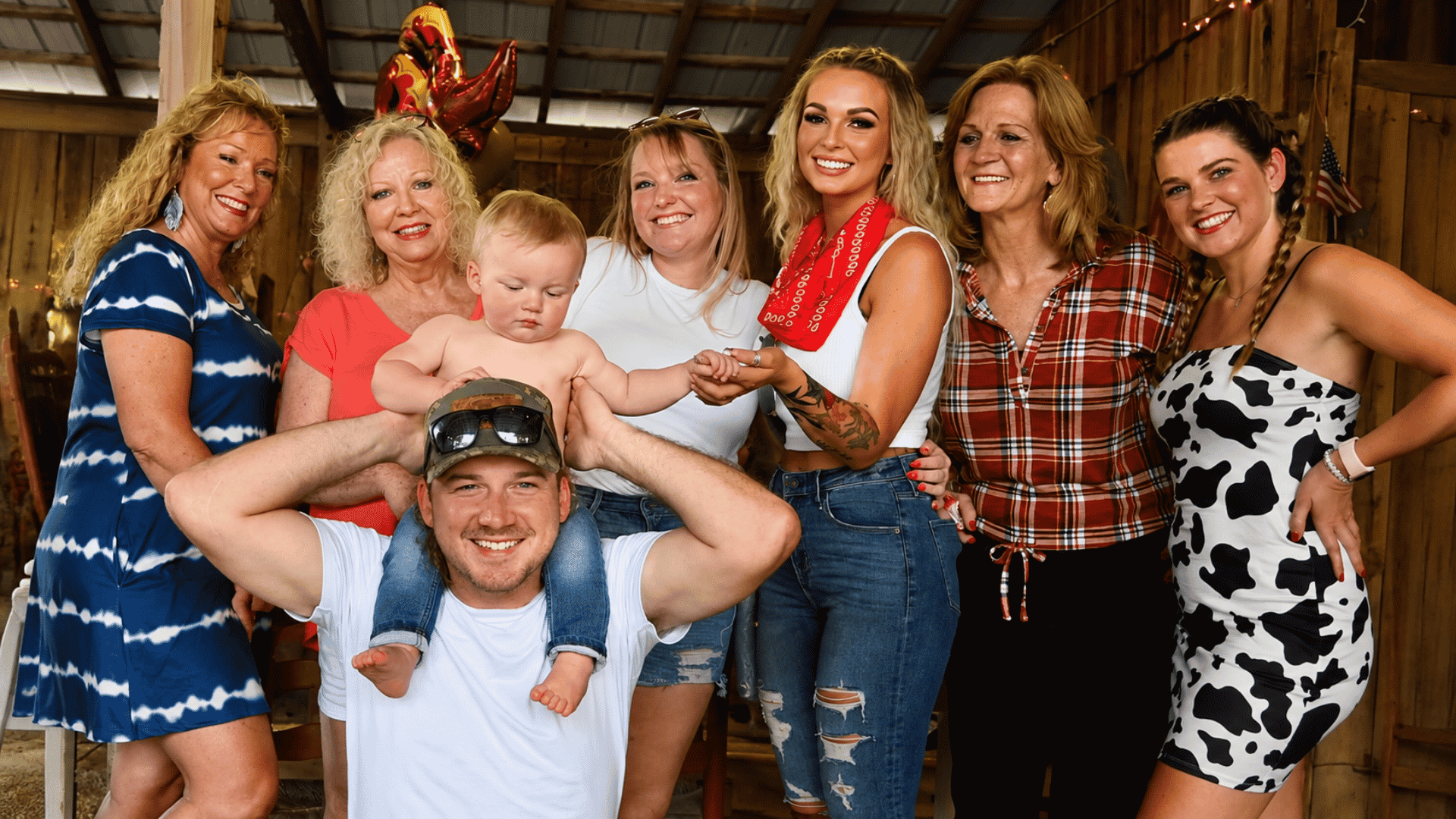 Morgan Wallen posing with his family and young son at a casual indoor gathering in a rustic barn setting.