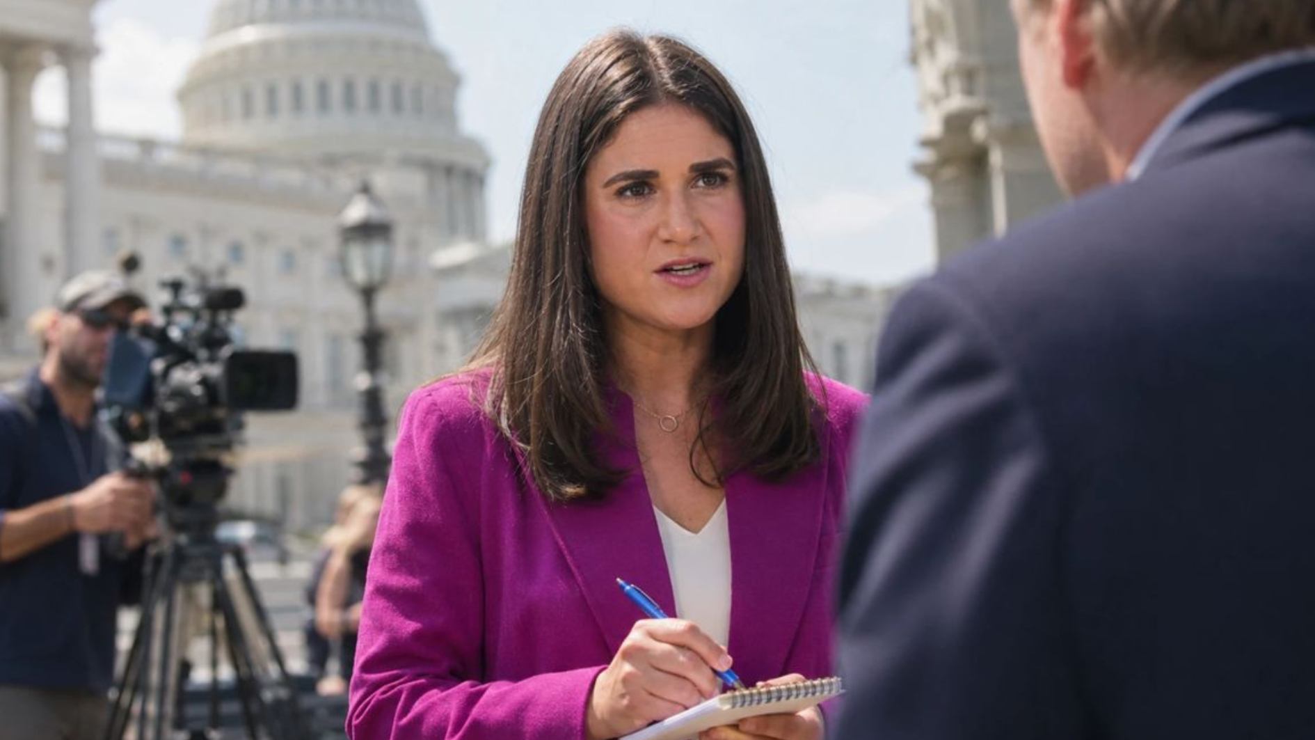 mychael schnell taking notes while reporting outside the u.s. capitol, with a camera crew in the background