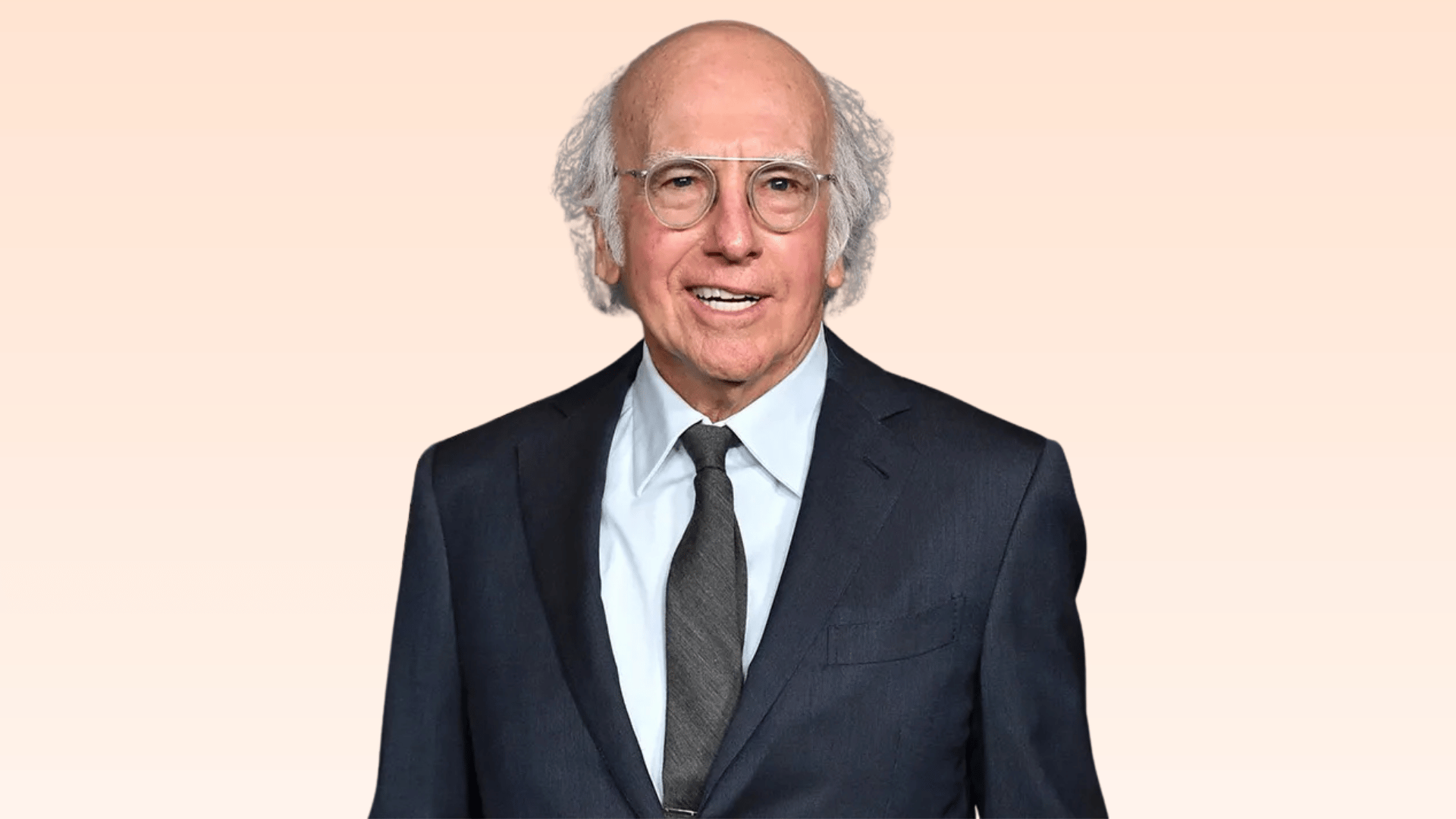 older man in a navy suit and glasses smiling against a soft beige background