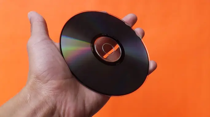 Hand holding a CD against a bright orange background