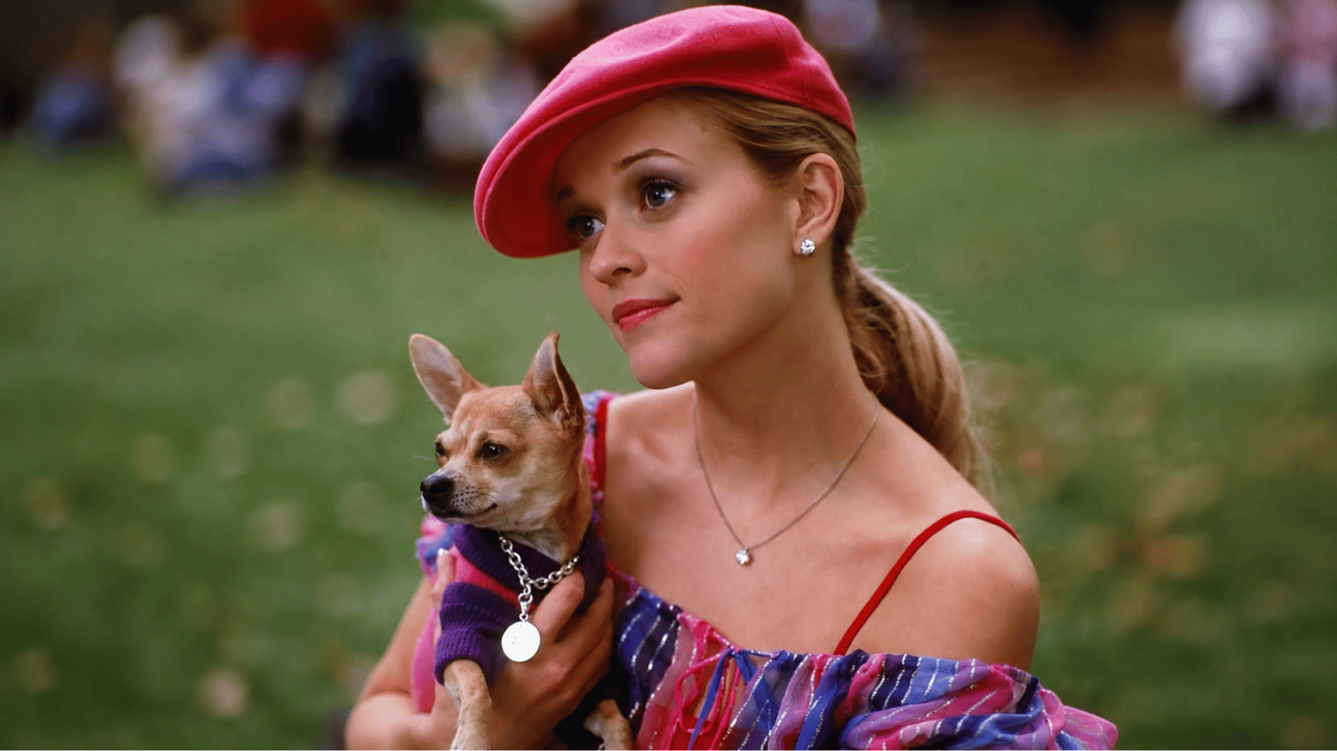 reese witherspoon in a pink cap holding a small dog during an outdoor portrait scene