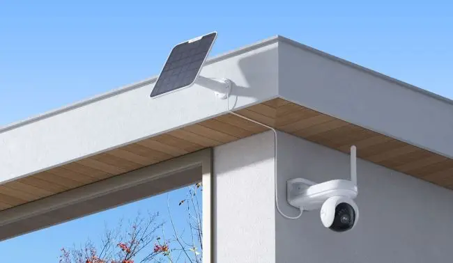 Outdoor security camera and solar panel mounted on modern house corner under clear blue sky