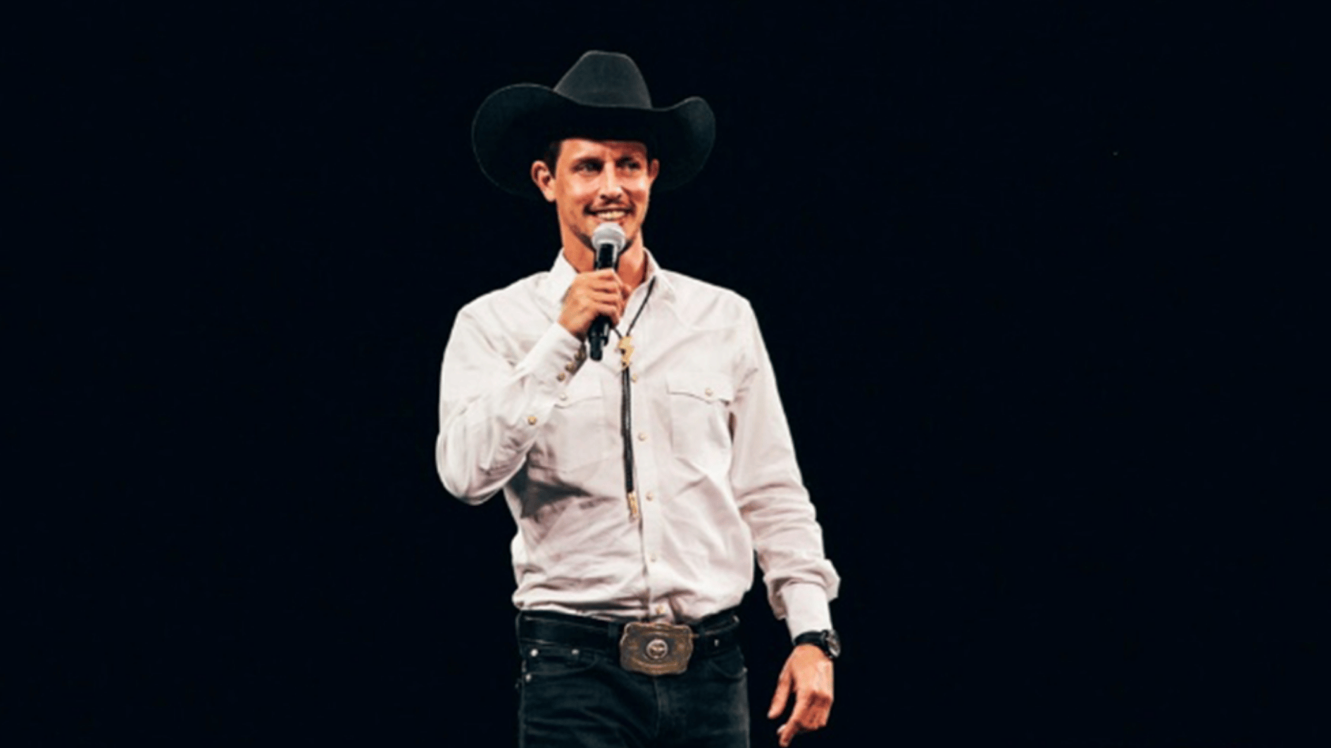 tony hinchcliffe wearing a cowboy hat and performing stand up comedy with a microphone onstage