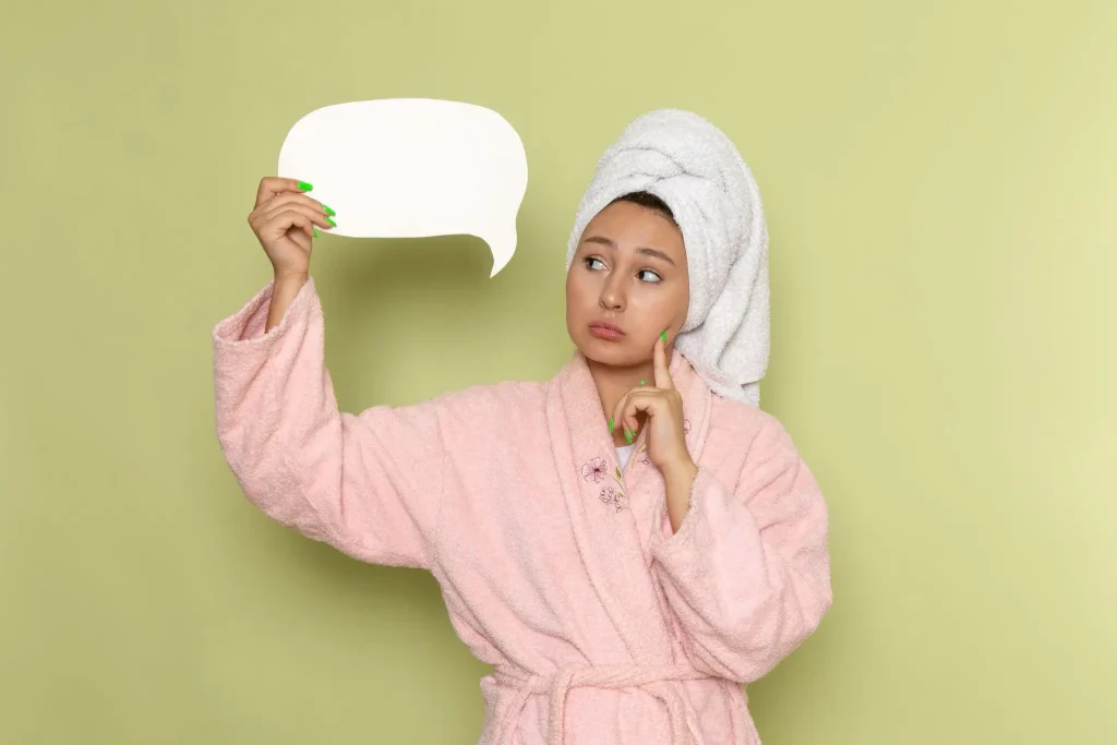 Woman in pink robe with towel on head holding blank speech bubble against green background