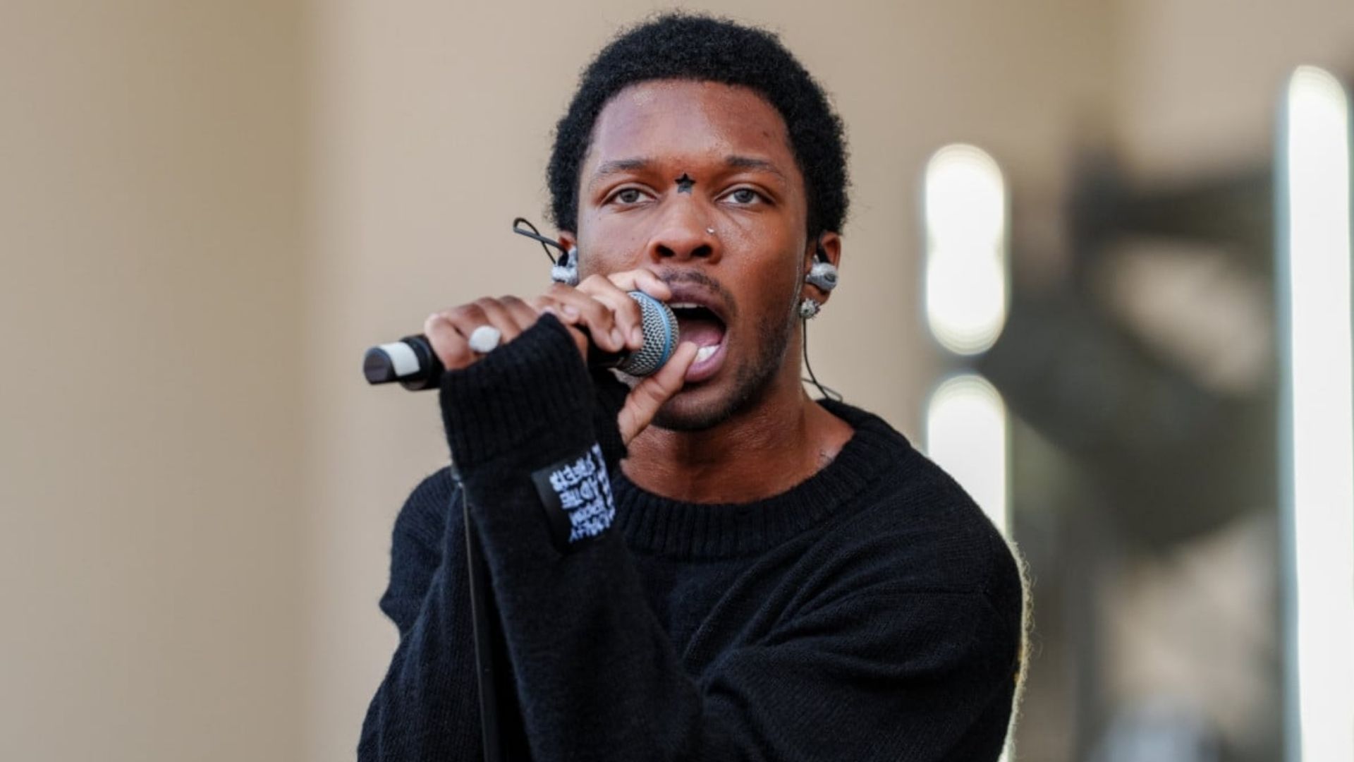 D4vd singer performing on stage while holding a microphone and wearing a black sweater.