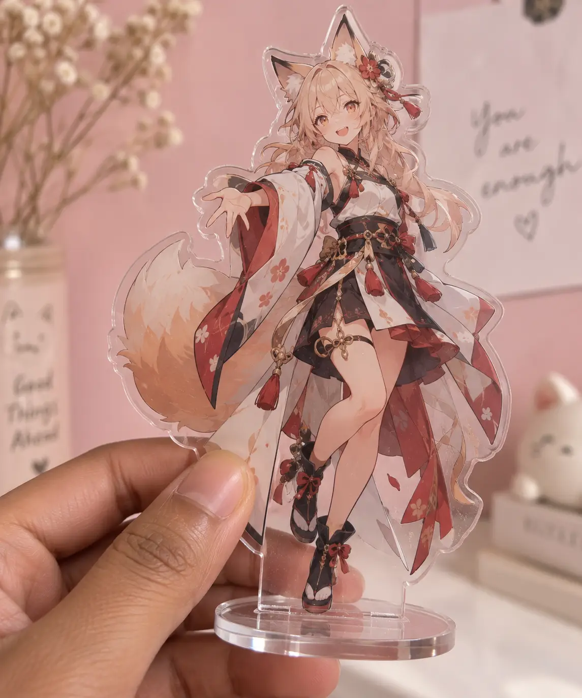 Hand holding anime character acrylic stand with floral kimono against pink background