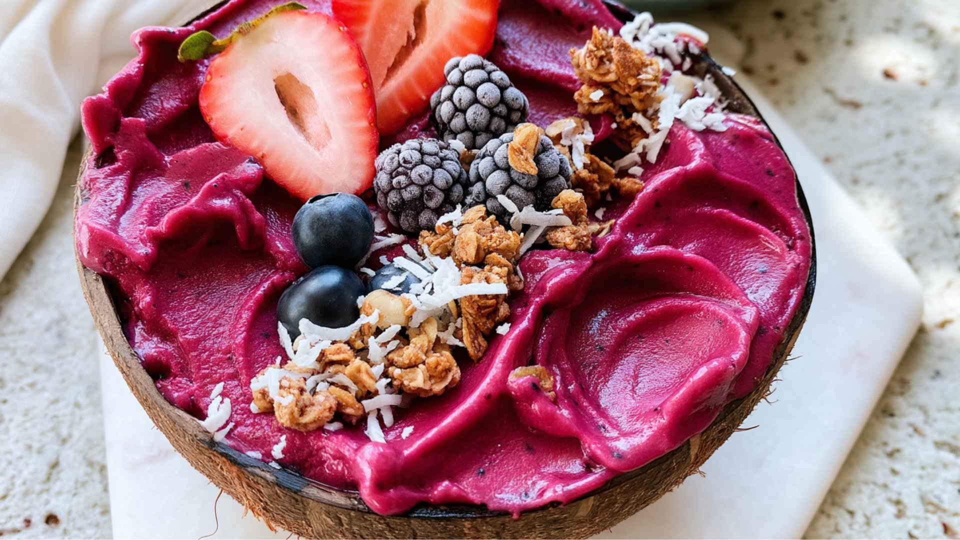 Acai bowl topped with strawberries, blueberries, kiwi, banana slices, coconut flakes, chia seeds, and granola on a rustic table.