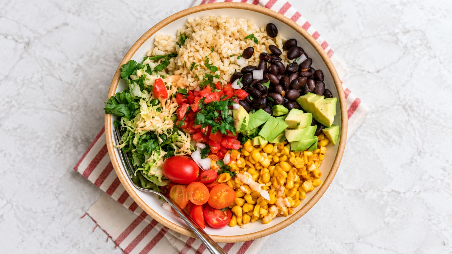 Black bean burrito bowl with brown rice, corn, tomato, lettuce, avocado, salsa and lime.