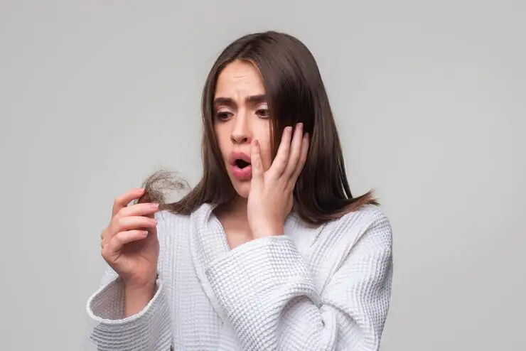 Woman in white bathrobe looking at hair in her hand with concerned expression