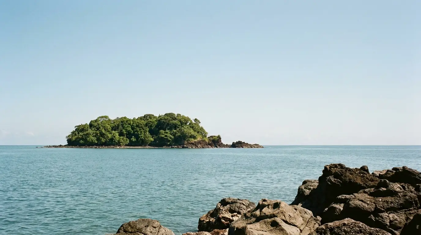 Remote tropical island with lush greenery surrounded by calm blue sea and rocky shoreline