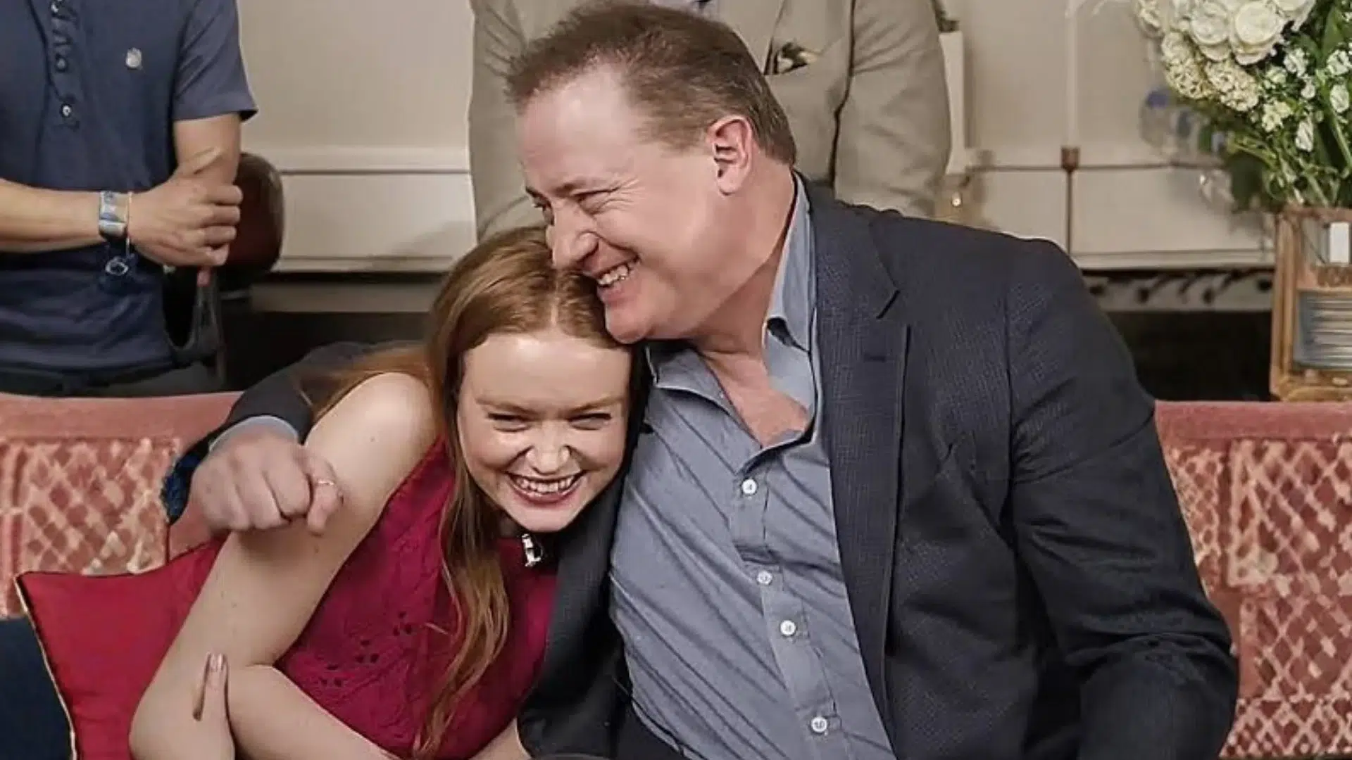young woman laughing as an older man hugs her while they sit together on a patterned sofa
