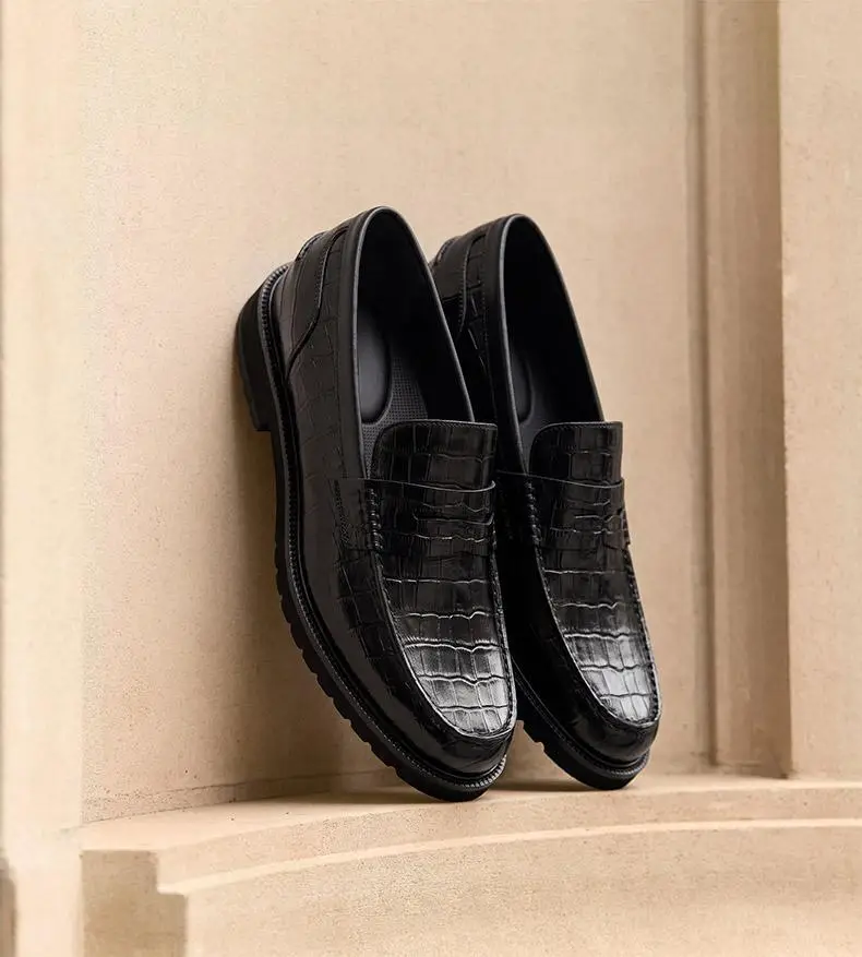 Black crocodile-pattern loafers on beige stone ledge in soft lighting