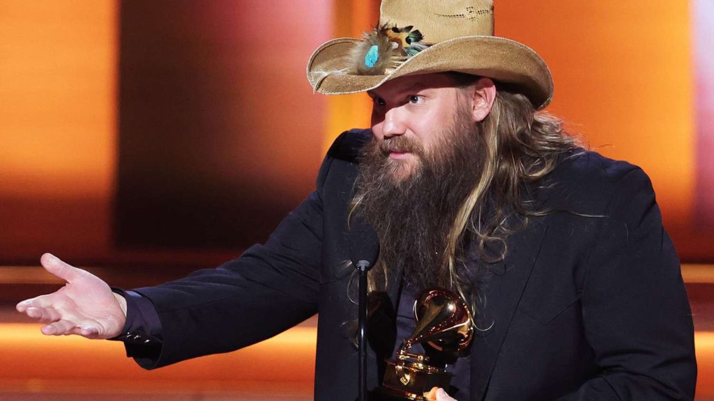Chris Stapleton in a suit and cowboy hat holding a Grammy Award
