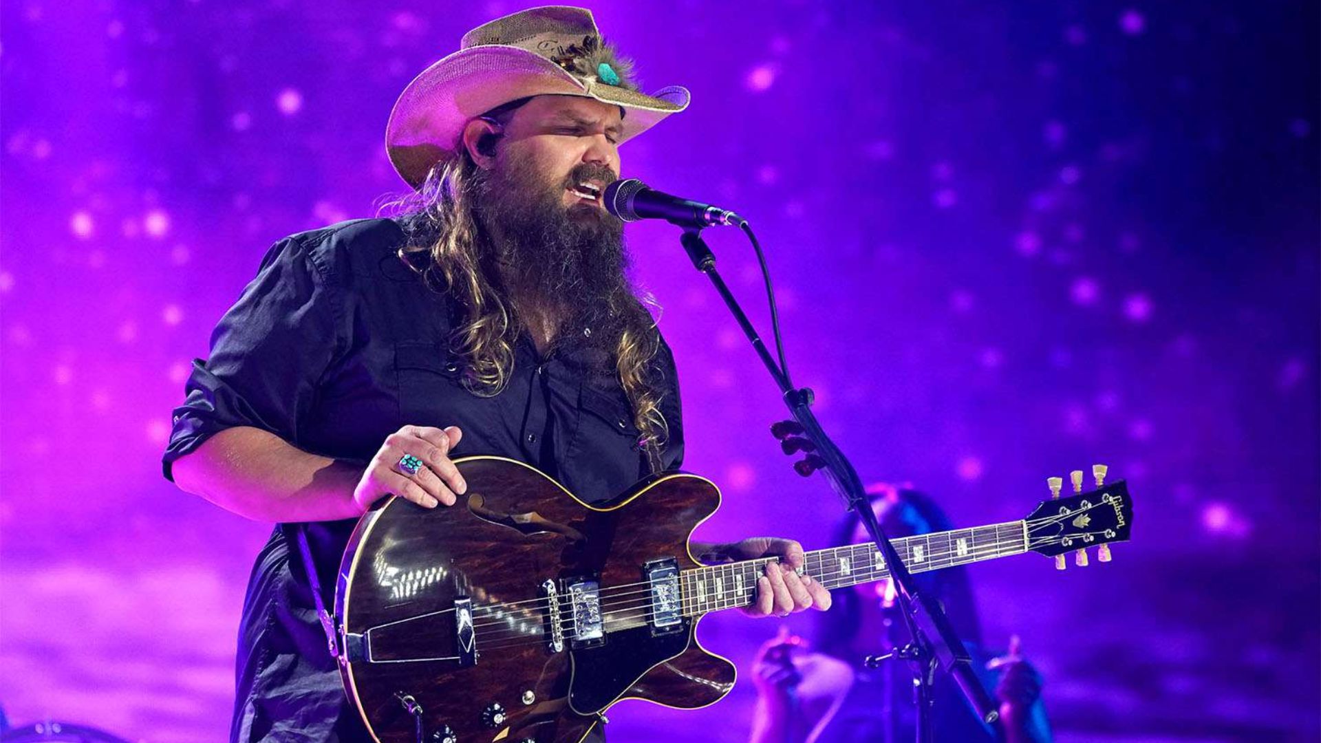 Chris Stapleton performing live on stage with a guitar under purple lights