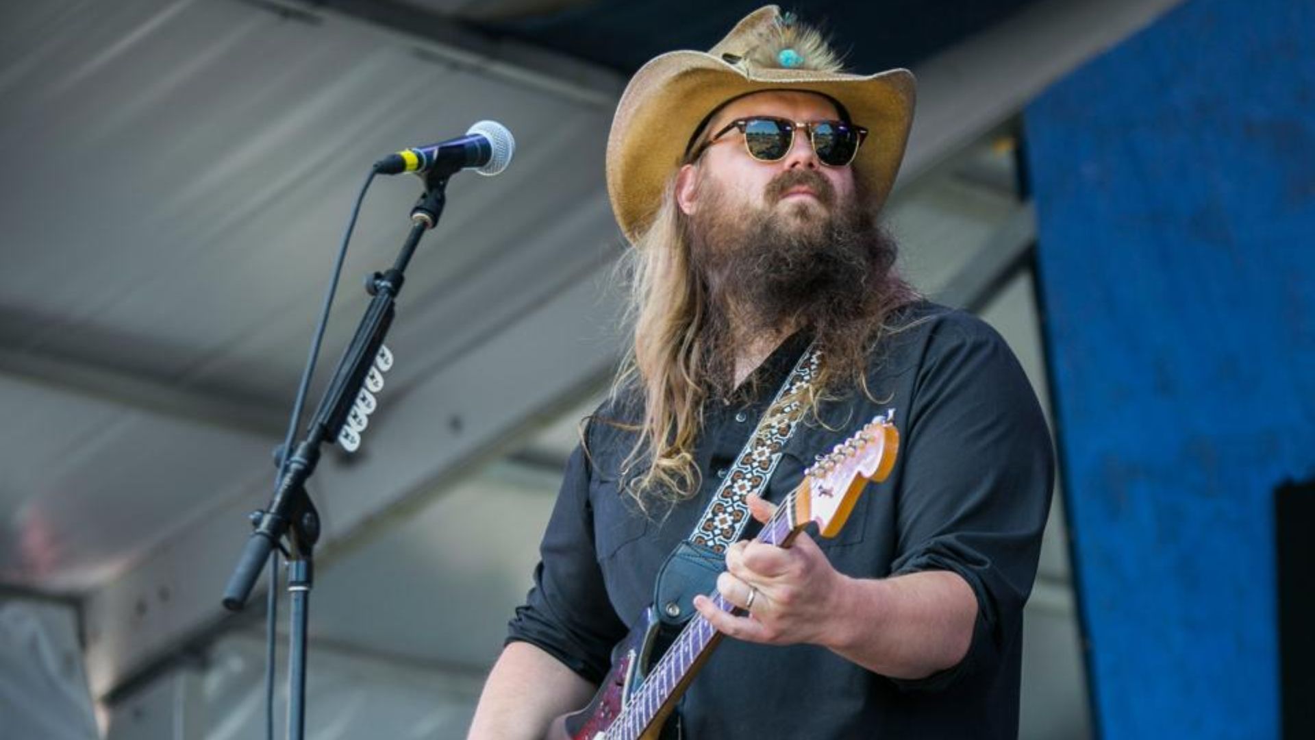 Chris Stapleton performing on an outdoor stage wearing a cowboy hat and sunglasses