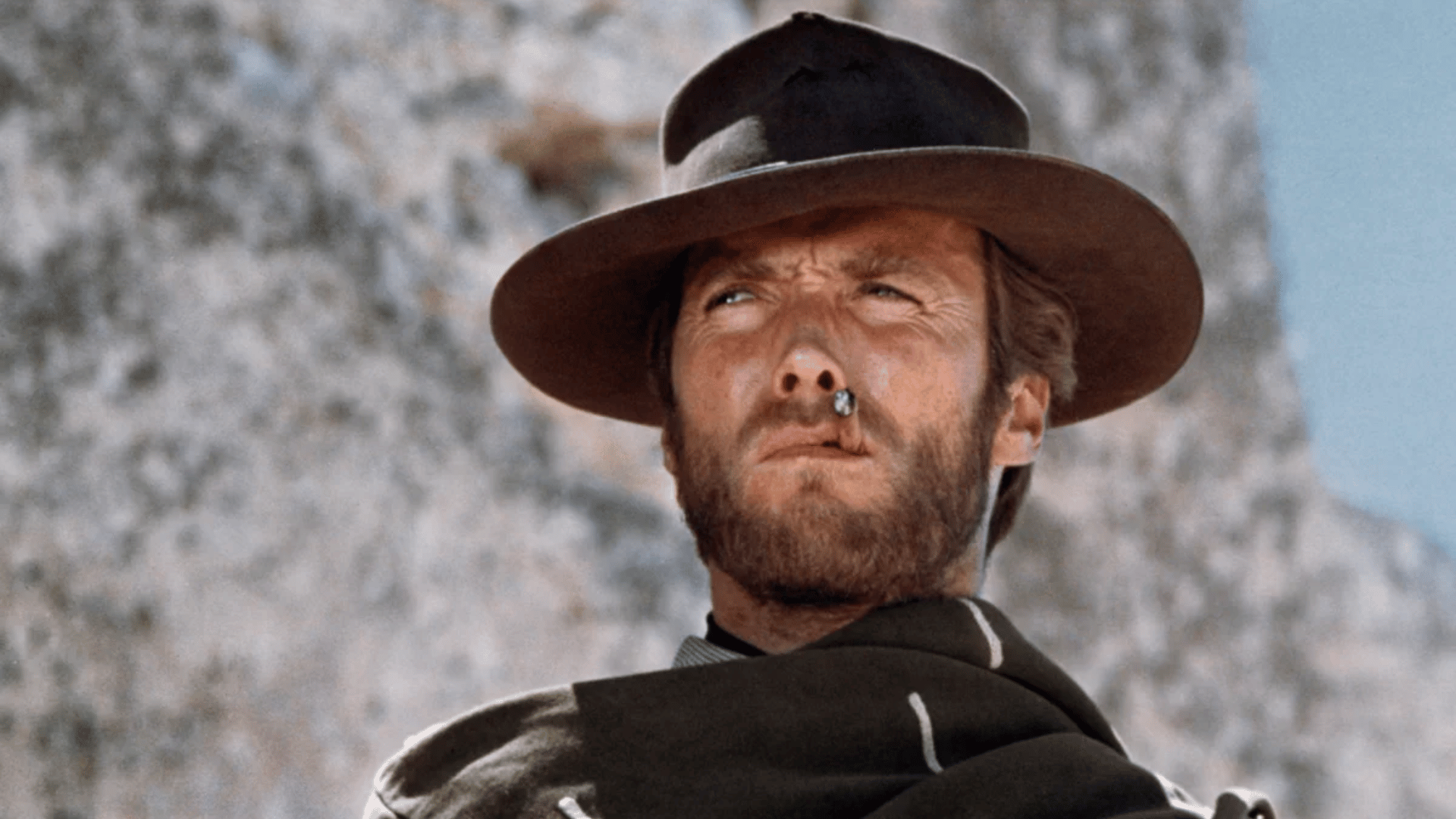 clint eastwood wearing a wide-brimmed cowboy hat and dark western clothing outdoors with a rugged desert landscape behind him