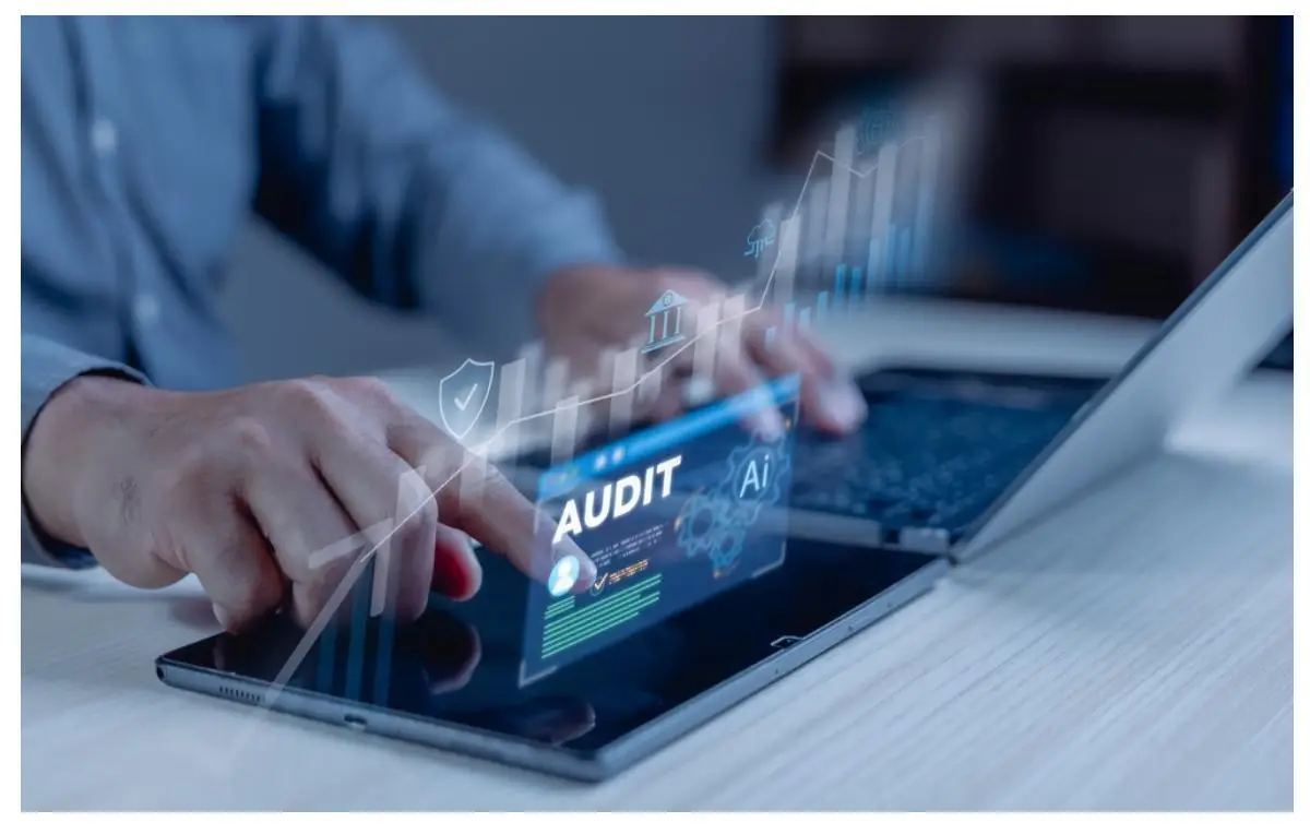 Hands interacting with holographic audit interface on digital tablet beside laptop in office setting