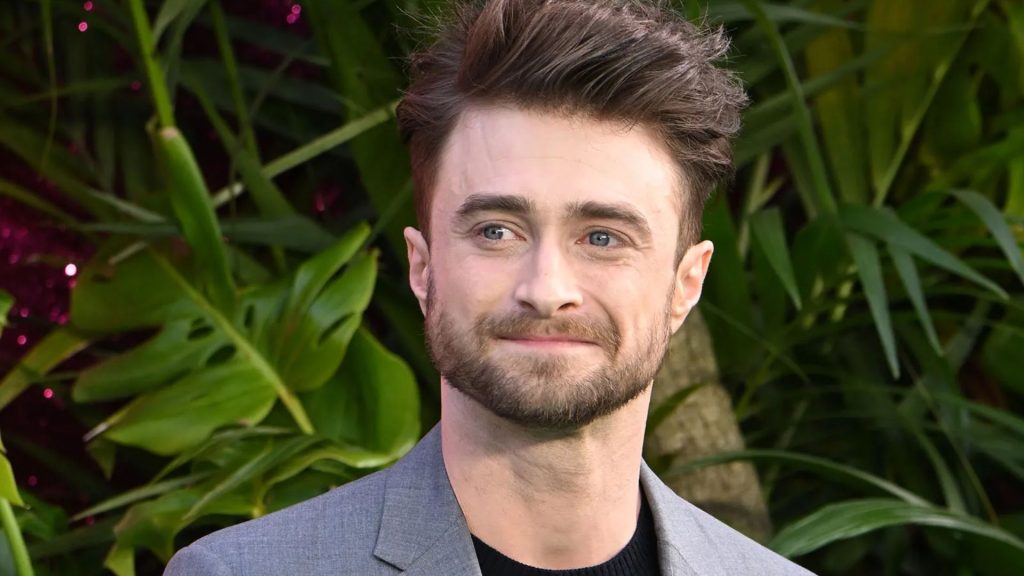 British actor Daniel Radcliffe in a grey suit smiling and posing at an event