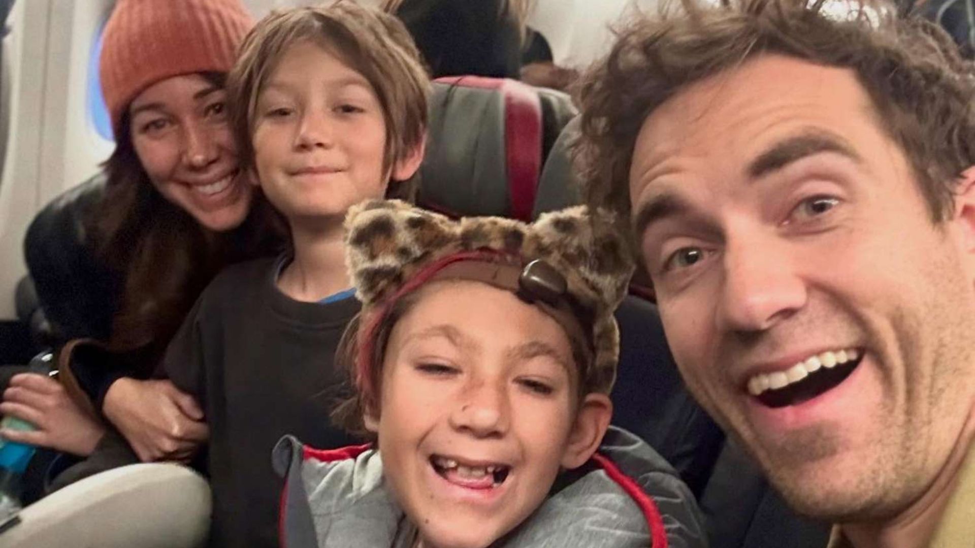 Danny Go smiling with his family during a selfie taken inside an airplane cabin.