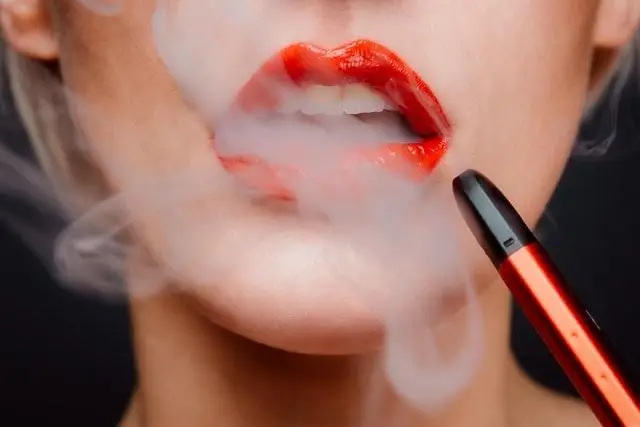 Red lips exhaling vapor from red vape pen in close-up shot