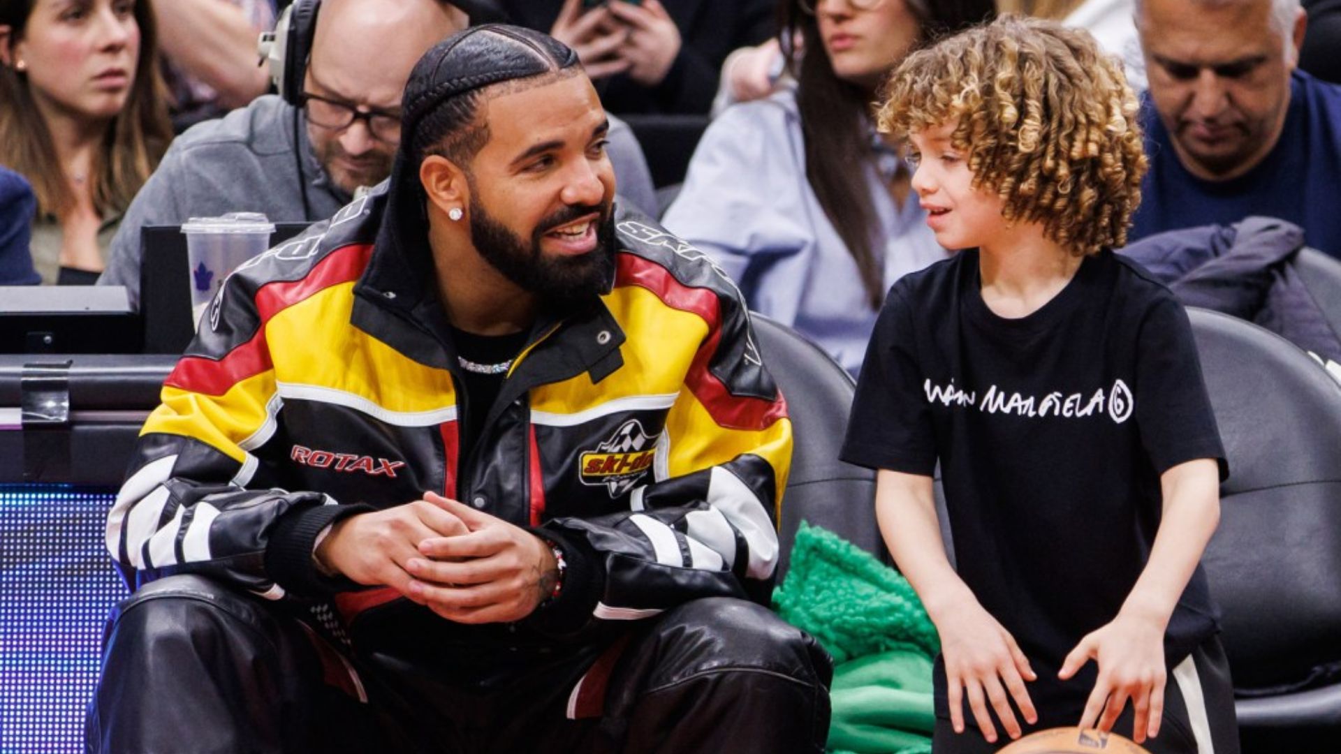 Drake sitting courtside with his son Adonis during a basketball game.