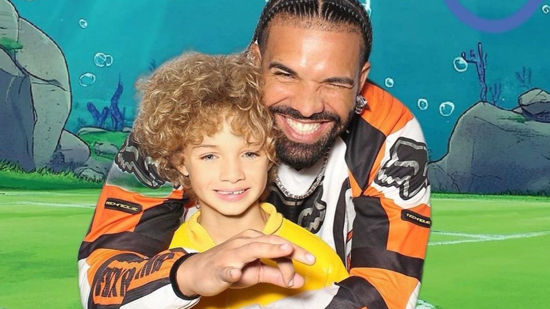 Drake smiling and posing with Adonis in front of a colorful background.